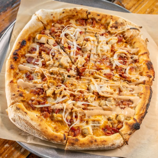 Whole chicken, bacon, and onion pizza with a creamy drizzle on parchment paper and a metal tray.