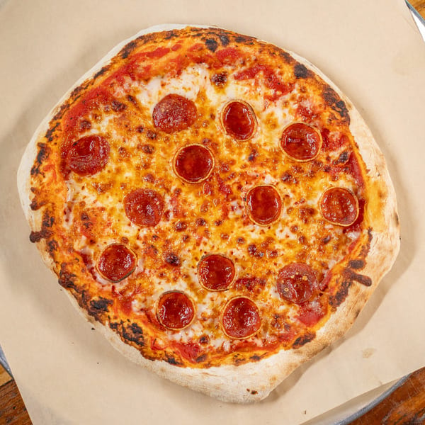 Round pepperoni pizza with melted cheese and a crispy crust on a metal tray.