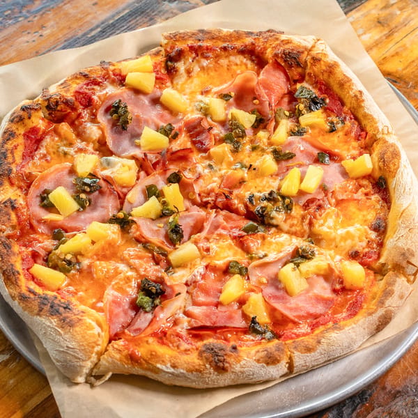 Hawaiian pizza with ham, pineapple, and jalapeños on a wooden table.