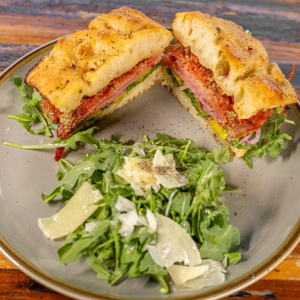 Focaccia sandwich with deli meats, peppers, and arugula, served with a side of parmesan arugula salad.