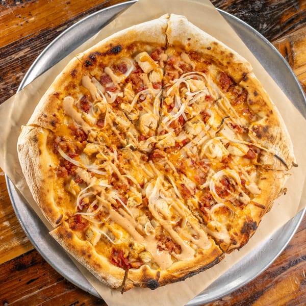 Chicken, bacon, and onion pizza with sauce drizzle on a metal tray over a wooden table.