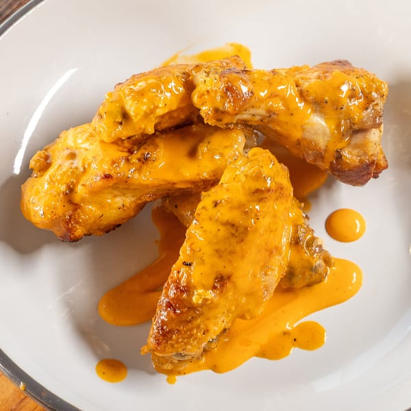 Four chicken wings covered in a creamy orange sauce, served on a white plate.