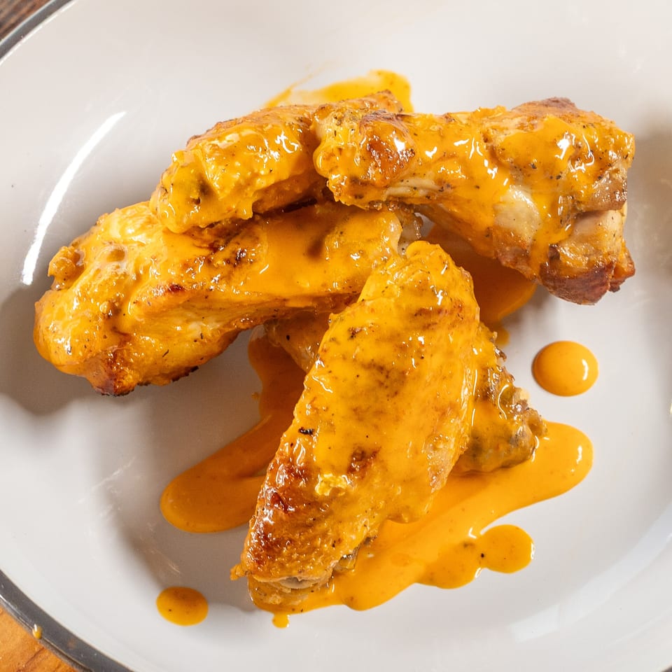 Four chicken wings covered in a creamy orange sauce, served on a white plate.