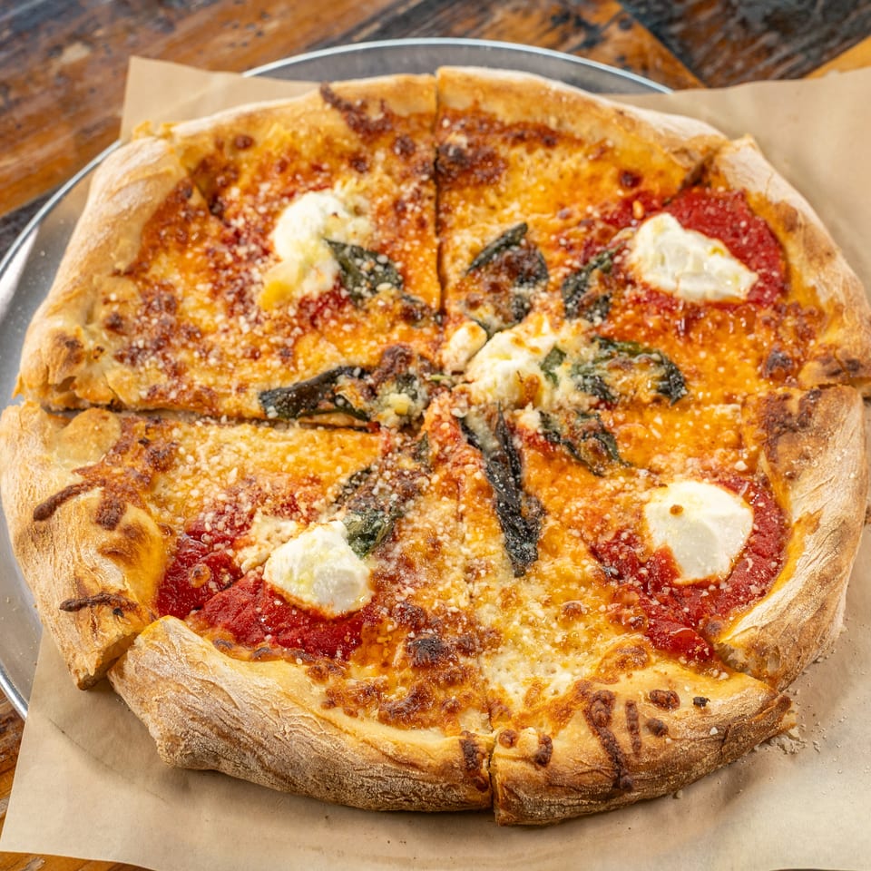 Sliced Margherita pizza with tomato sauce, mozzarella, basil, and dollops of ricotta on a metal tray.